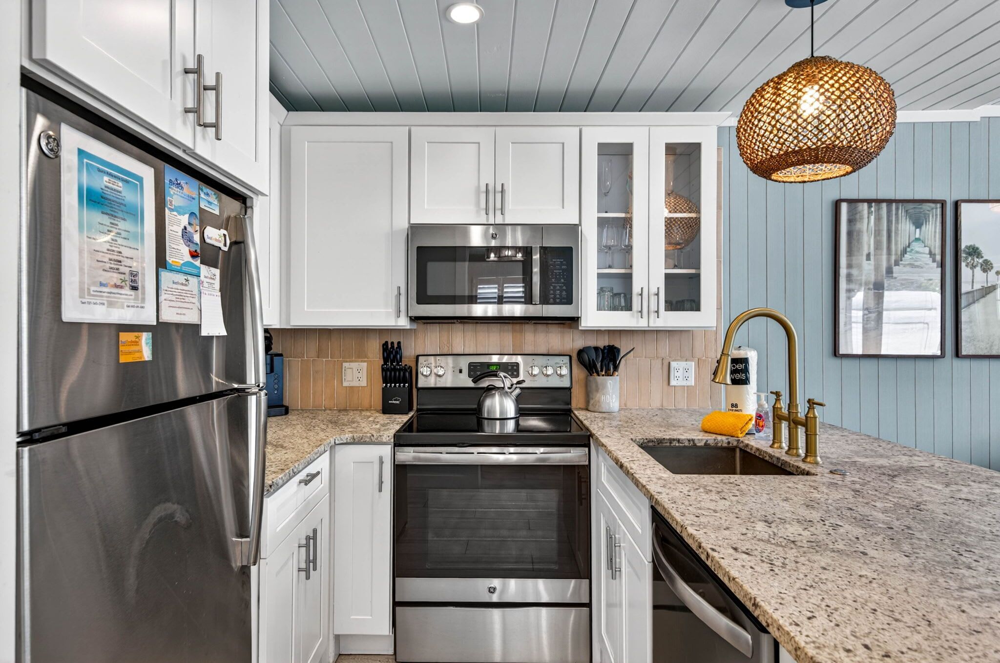 A kitchen with stainless steel appliances, white cabinets, a granite countertop, and a hanging light fixture.