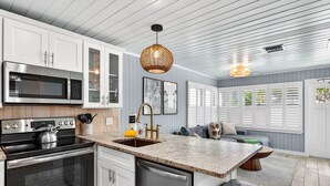 A modern kitchen with white cabinets, stainless steel appliances, a granite countertop, and a hanging light fixture. - Island Vibes House Steps from Clearwater Beach (Clearwater Beach)