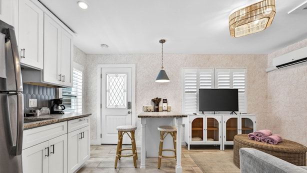 A kitchen with white cabinets, a central island with stools, a TV, and a wicker sofa. - Island Vibes Cottage Near Clearwater Beach (Clearwater Beach)