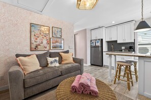 A modern kitchen with white cabinets, a stainless steel refrigerator, and a bar area with stools. - Island Vibes Cottage - Amazing Location (Clearwater Beach)