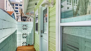 A narrow wooden deck leading to a door with a window, surrounded by light green walls and a white fence with decorative cutouts. - Island Vibes Cottage Near Clearwater Beach (Clearwater Beach)