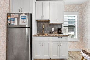 A kitchen with white cabinets, a stainless steel refrigerator, a window with blinds, and a patterned wallpaper. - Island Vibes Cottage - Amazing Location (Clearwater Beach)