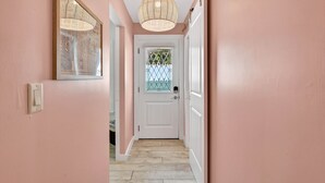 A hallway with pink walls, a white door with a decorative glass panel, and a woven ceiling light fixture. - Island Vibes Cottage Near Clearwater Beach (Clearwater Beach)