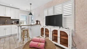 A modern kitchen with white cabinets, a large flat-screen TV, and a wicker seating area. - Island Vibes Cottage Near Clearwater Beach (Clearwater Beach)