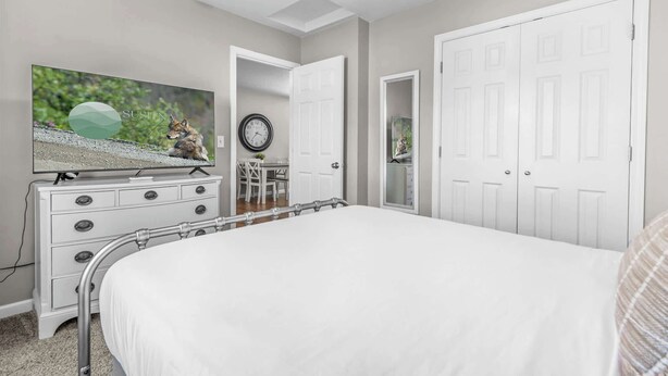 Une chambre à coucher avec un grand lit, une commode à tiroirs, un téléviseur, une horloge et une porte.