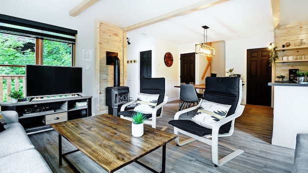 Ett modernt vardagsrum med TV, sittmöbler, en öppen spis och utsikt över grönområden.