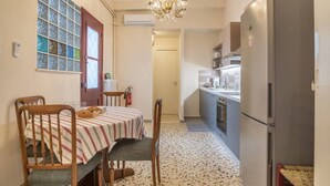 A compact kitchen with a refrigerator, a dining table with chairs, a chandelier, and a window with stained glass. - 4 Guests - Veneris Residence Apartment in Chania (Chania)