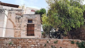 A stone building with a wooden door, a stone wall in the foreground, and a tree with green foliage. - 4 Guests - Veneris Residence Apartment in Chania (Chania)