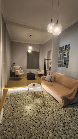 A living room with a sofa, a coffee table, and a dining area with chairs and a table. - 4 Guests - Veneris Residence Apartment in Chania (Chania)