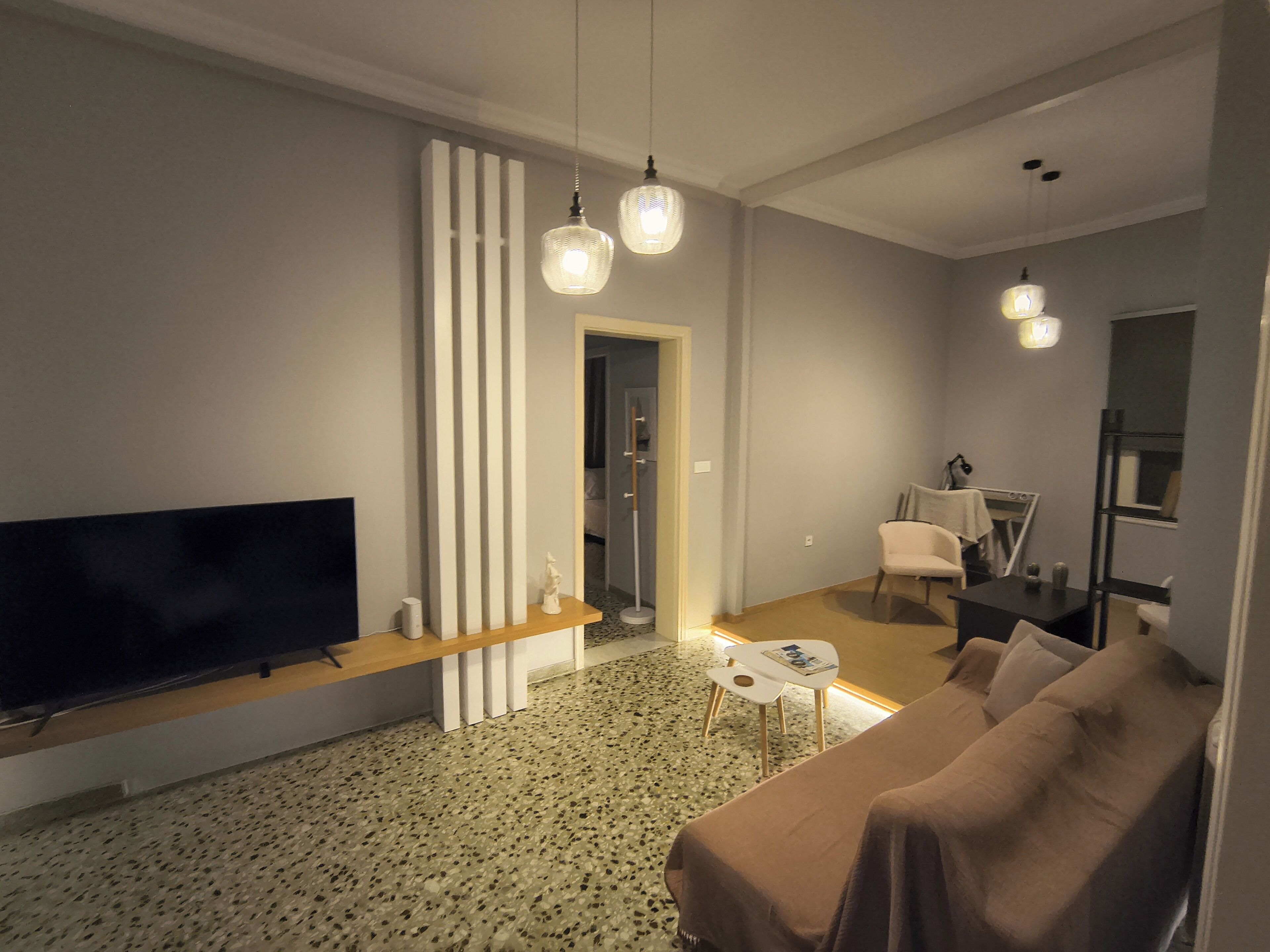 Een moderne woonkamer met een flatscreen televisie, een bank, een salontafel, en een eethoek met een stoel en tafel.