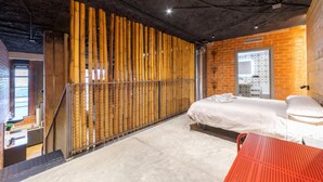 Ett modernt hotellrum med en säng, en röd stol, en avskärmning av bambu och en tegelvägg.
