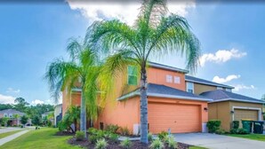 Una casa residencial con garaje, césped cuidado y palmeras.
