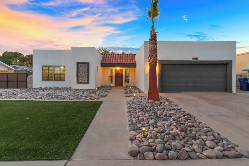 Una casa moderna con garaje, césped cuidado y un camino bordeado de rocas.