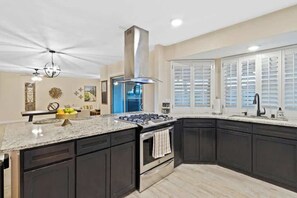 A modern kitchen with dark cabinetry, a central island, a built-in oven, and a stainless steel range hood. - Eastside Spanish Castilla (El Paso)