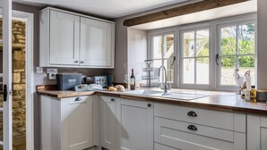 A kitchen with white cabinets, a wooden countertop, a built-in oven, and a window with a view of the outside. - Old Stable Cottage, Kingham, Chipping Norton (Kingham)