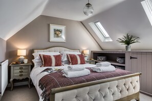 A bedroom with a bed, bedside tables, a lamp, a framed picture, a plant, and a skylight.
