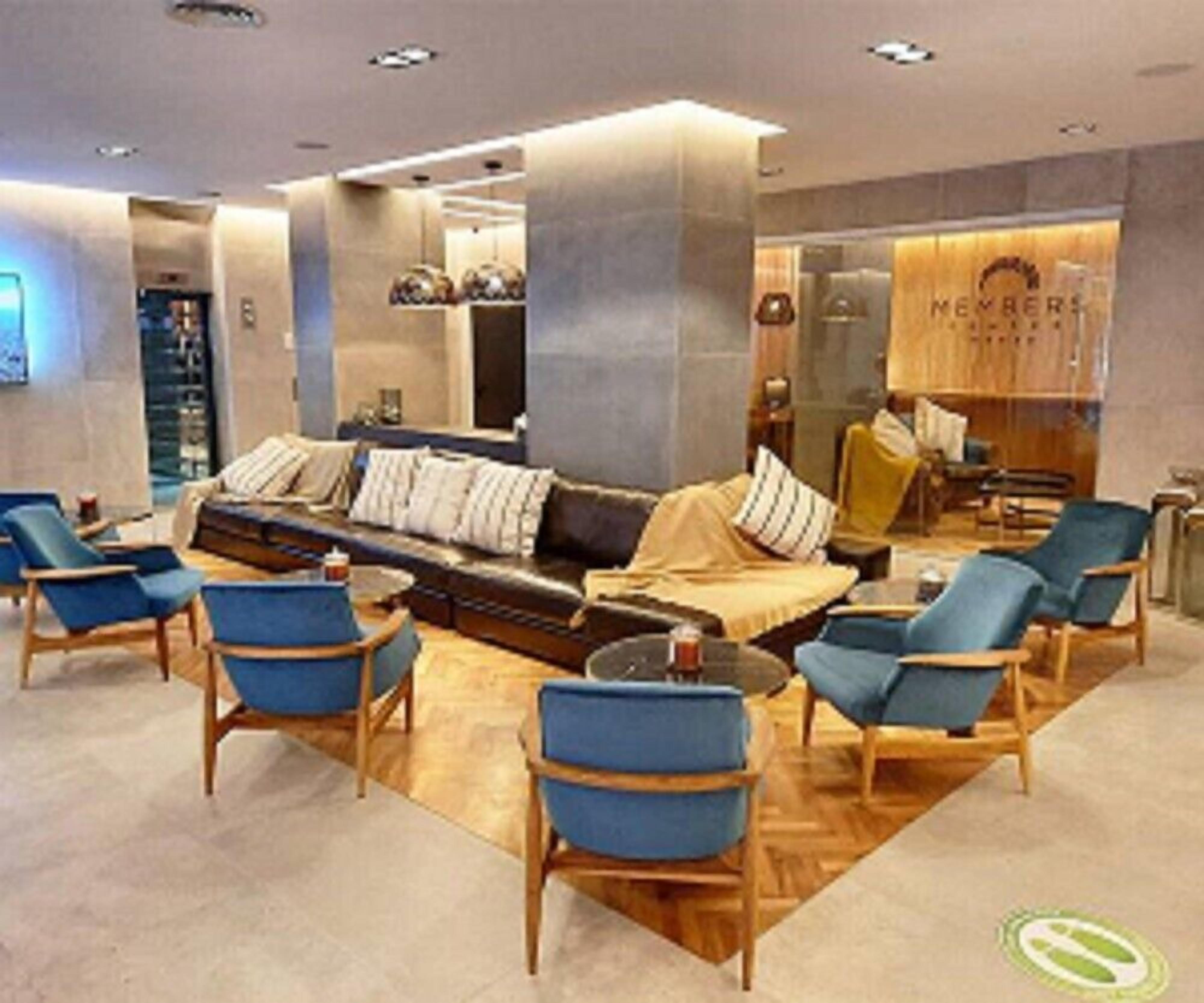 Un hall d’entrée moderne avec un canapé et des fauteuils, un comptoir d’accueil et une enseigne indiquant « MÉMBRES ».