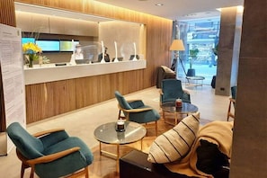 A modern reception area with a wooden reception desk, teal armchairs, and a sofa with striped cushions.