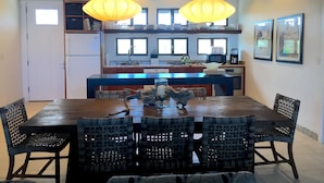 A dining area with a wooden table and wicker chairs, a kitchen with a central island, and pendant lighting. - Private Home on Amazing Beach! 22 Steps to Beach!  (Coconut Bay)