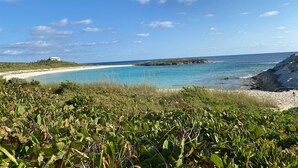 A coastal landscape with a sandy beach, clear blue waters, and a white building on a hill. - Private Home on Amazing Beach! 22 Steps to Beach!  (Coconut Bay)