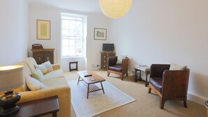Una sala de estar con sofá, sillón, mesa de centro y televisor sobre un mueble.