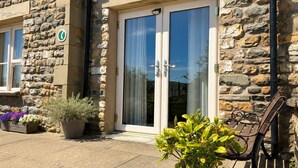 A stone building with a glass door, potted plants, and a bench outside. - Howgills Apartment 8 (self-catering accommodation with free parking and Wi-Fi) (Sedbergh)