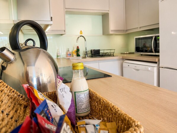 A kitchen with a kettle, a bottle of milk, and various food items on the counter.