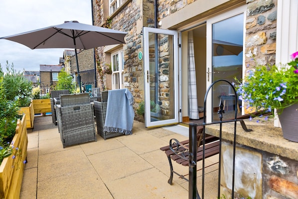 Une terrasse extérieure avec des meubles en osier, une table et un parasol.