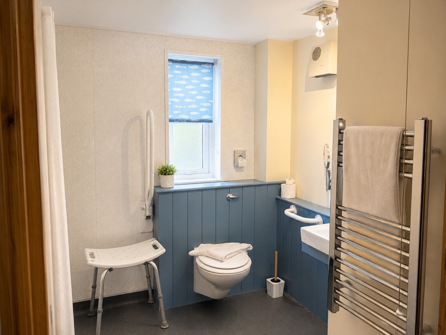 A bathroom with a toilet, bidet, towel rack, and a small window with a plant.