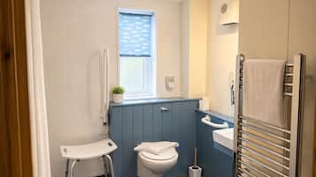 A bathroom with a toilet, bidet, towel rack, and a small window with a plant.