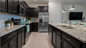 Une cuisine moderne avec des meubles de couleur sombre, des appareils en acier inoxydable, des plans de travail en granit et des luminaires suspendus.