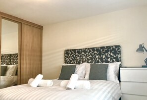 Una cama bien hecha con almohadas y toallas, un armario de madera, cabecera con diseño geométrico y una lámpara de noche.