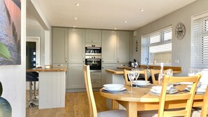 A modern kitchen with grey cabinets, a wooden dining table set for four, and a clock on the wall. - 16 Beatrice Avenue, Shanklin, isle of Wight (Shanklin)