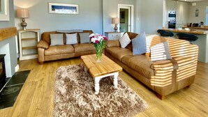A living room with a brown leather sofa, a wooden coffee table, and a fluffy rug. There is a kitchen in the background with a microwave and a kettle. - 16 Beatrice Avenue, Shanklin, isle of Wight (Shanklin)