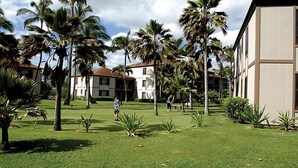 A courtyard with palm trees, a grassy lawn, and a building with a beige facade. - Pono Kai Resort - 1 Bedroom (Kapaa)