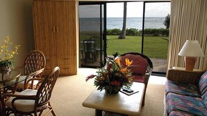 A room with a view of the ocean, a wicker chair, a table with a vase of flowers, and a sofa. - Pono Kai Resort - 1 Bedroom (Kapaa)
