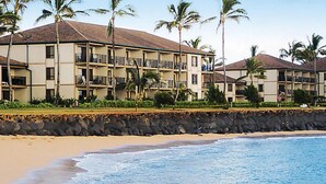 A beachfront hotel with multiple balconies, palm trees, and a sandy beach. - Pono Kai Resort - 1 Bedroom (Kapaa)