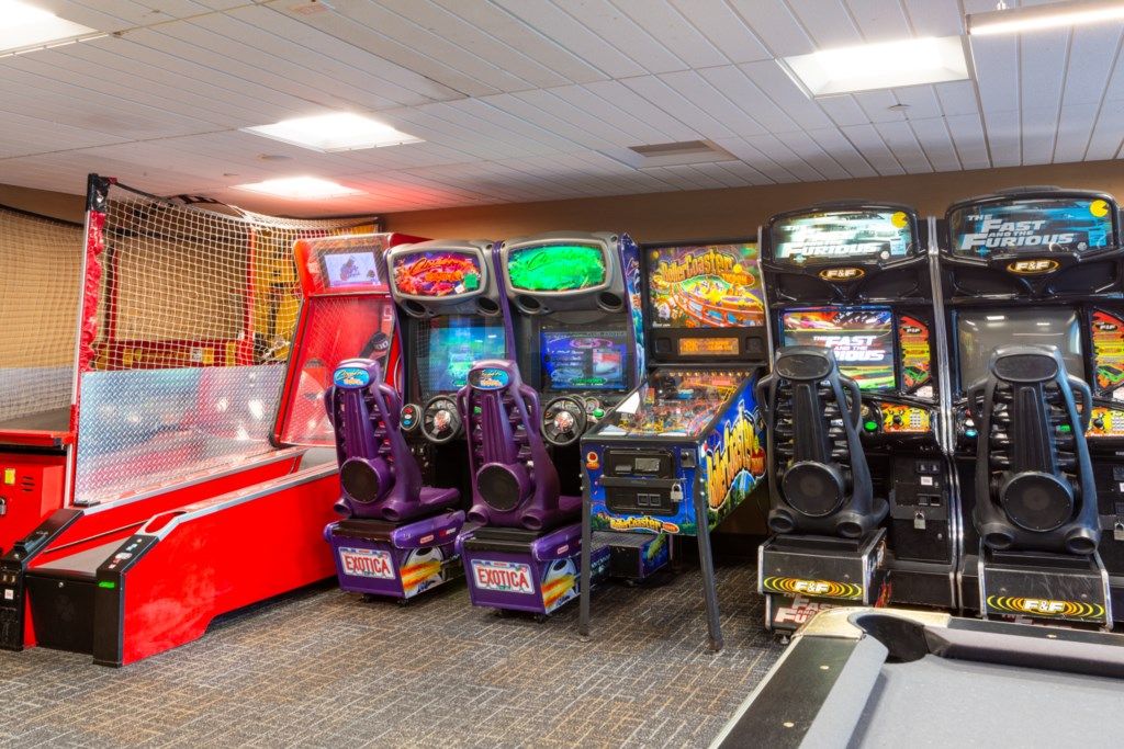 A row of arcade games, including 'The Fast and the Furious' and 'Exotica' machines, in a room with a red play area and a netted enclosure.