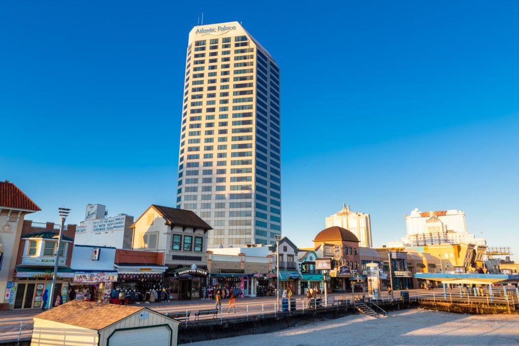Un hotel alto de diseño moderno, rodeado de una calle animada con diversas tiendas y un paseo marítimo.