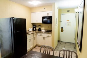 Compact kitchen area with a refrigerator, microwave, and coffee maker, along with a table and chair.