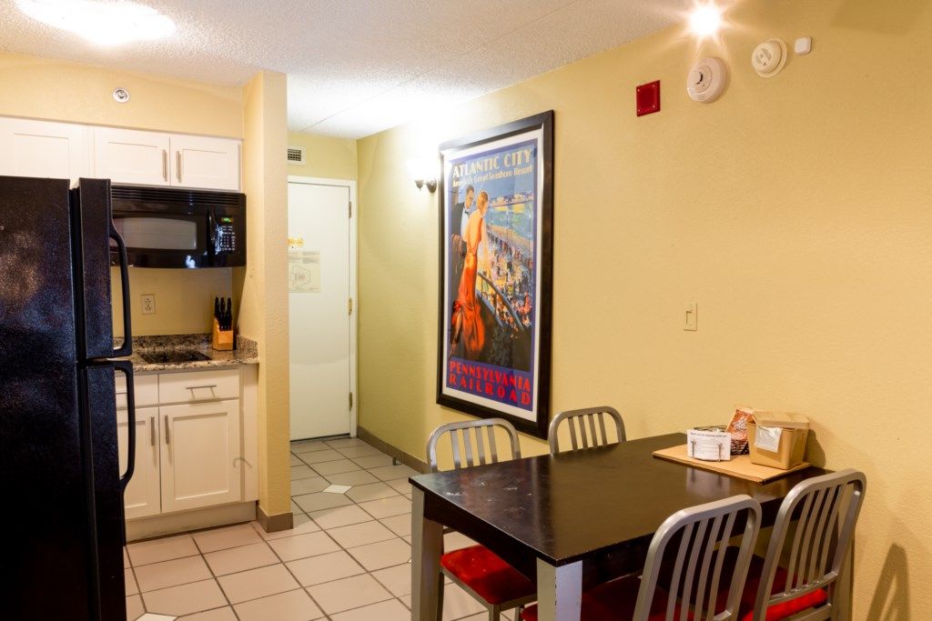 A compact kitchen with a refrigerator, microwave, and cabinets. There's a dining table with chairs and a poster on the wall.