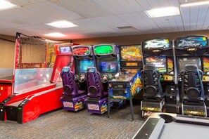 Une rangée de jeux d’arcade, dont les machines « The Fast and the Furious » et « Exotica », dans une pièce dotée d’un espace de jeu rouge et d’un enclos grillagé.