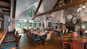Un'ampia sala da pranzo con tavoli e sedie in legno, grandi finestre e un camino in pietra.