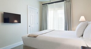 Une chambre d’hôtel avec un lit, un téléviseur fixé au mur, une porte et une fenêtre avec des rideaux.