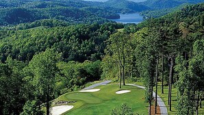 Un campo da golf con bunker in sabbia, una distesa d'acqua sullo sfondo e colline ricoperte da fitti boschi.