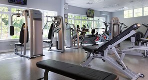 Une salle de sport équipée de machines Nautilus, dotée de grandes fenêtres et d’un téléviseur fixé au mur.