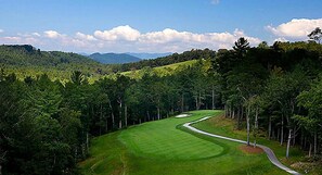 Un parcours de golf avec un sentier sinueux, entouré d’une forêt dense et bordé de collines en arrière-plan.