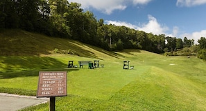 Een golfbaan met een bord waarop afstanden in yards staan vermeld, aangegeven in verschillende kleuren op kunstgras.