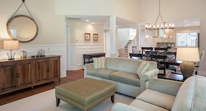 A living room with a sofa, ottoman, and a wooden cabinet. There is a staircase in the background leading to another room.