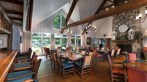 A spacious dining area with wooden tables and chairs, large windows, and a stone fireplace. - Club Lodges at Trillium - 3 Bedroom Presidential (Cashiers)